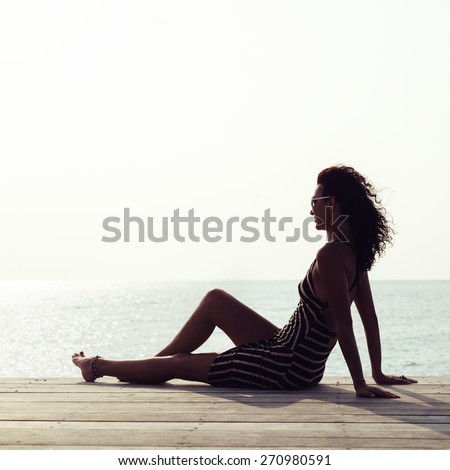 Young sexy woman relaxing alone on the pier near the sea and looking on the water and waiting for somebody in ocean