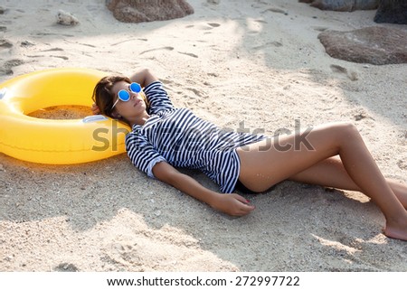 Beautiful woman in sunglasses lying on a beach in sand at summer day. Outdoor lifestyle portrait of girl