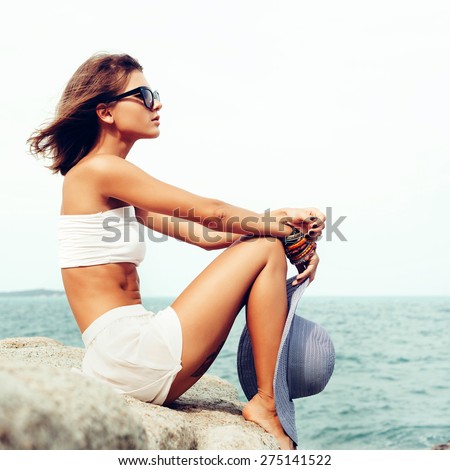 Sunny fashion portrait of pretty young sensual woman posing on the rocks alone on the ocean seashore. Outdoors lifestyle portrait