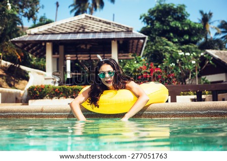 Young pretty fashion woman body posing in summer in pool with clear water lying on mattress in color bikini and having fun