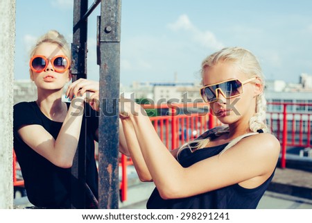 portrait of two pretty hipster blonde sisters  wearing plaid skirt and  black T-shirt. Girls smile, have fun against  urban city.