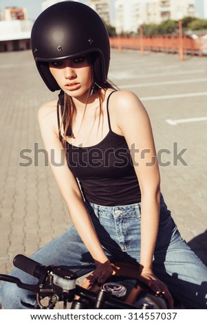 Biker girl in helmet sitting on vintage custom  motorcycle looking at the camera. Outdoor lifestyle portrait