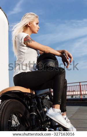 Biker girl with helmet sitting on vintage custom motorcycle. Outdoor lifestyle portrait