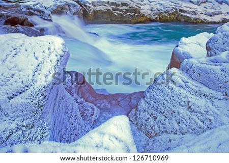 Winter landscape image of thick white frost on rocks along mountain creek cascading clean cold water.