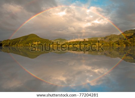 Full rainbow over forest with mirror-like reflection