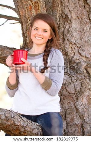 Young Woman Drinking Coffee - This is a photo of a cute you woman sitting in a tree enjoying a cup of coffee. Shot with natural light and a shallow depth of field.