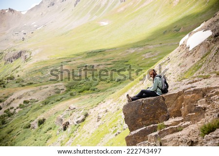 Female Hiker Sitting On Cliff - This is a shot of a young woman hiker sitting down on a cliff enjoying the view of her hike.