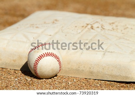 This is a high contrast shot of an old baseball sitting next to a dirty base on a baseball field.