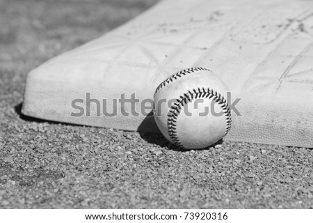 This is a high contrast, black and white image of an old baseball sitting next to a base on a baseball field.