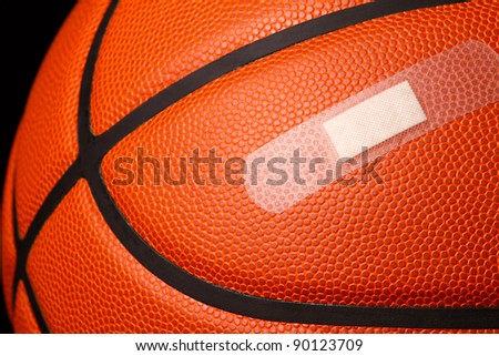 This is a close up photo of a basketball with a band-aid shot on a black background. Sports injury concept.