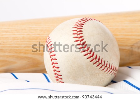 This is a shot of an old baseball sitting on a baseball jersey next to an old wooden bat. Shot with a shallow depth of field.