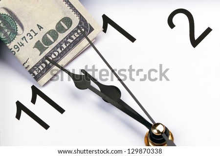 time is money. hour hand points to the U.S. hundred dollar bill.