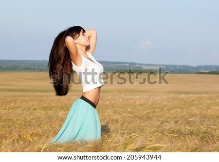 young beautiful long haired girl in a skirt and blouse posing on a background field with ears. Side view.  Photo toned light yellow to give summer atmosphere