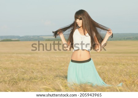 young beautiful long haired girl in a skirt and blouse posing on a background field with ears. Photo toned light yellow to give summer atmosphere