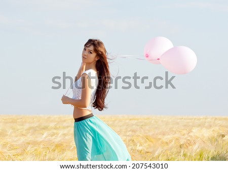 young beautiful long haired girl with balloons in hand posing on a background field with ears.back view.