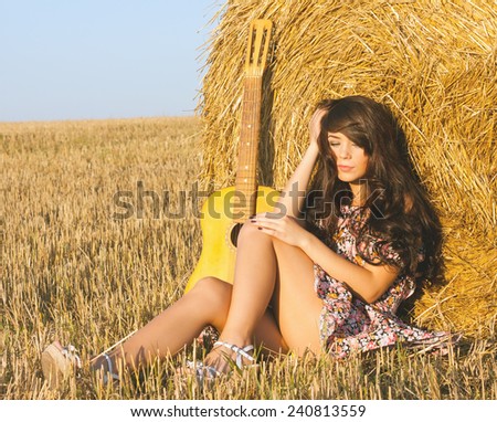 Beautiful country girl in short dress on a summer day basking in the field on a background of haystack.toned