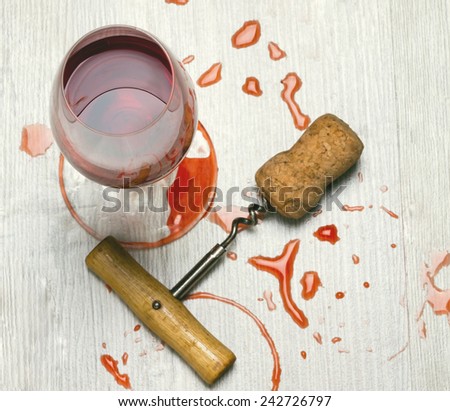 glass of wine and a corkscrew with cork wood surface with stains from wine.toned