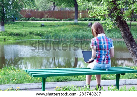teen girl working on a laptop while sitting on a bench outdoors.\
back view
