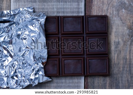 Open the foil-wrapped chocolate bar lying on a wooden surface.top view