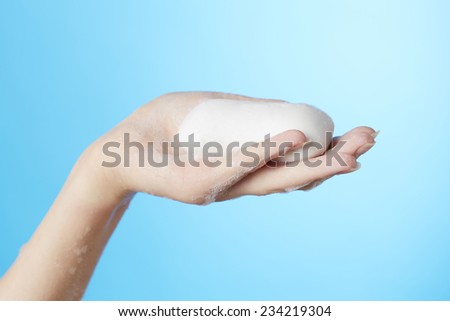 Woman\'s hand in foam of shower gel with soap on blue background
