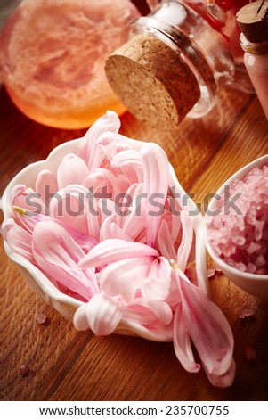 Spa still life with pink sea salt and flower petals on wooden background