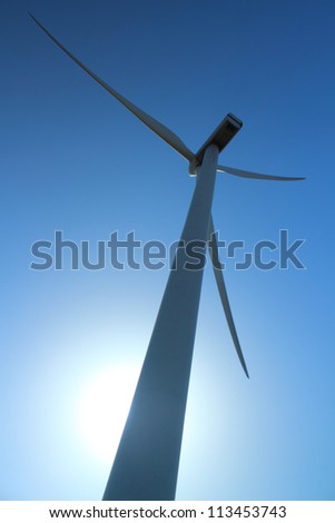 Wind power station - wind turbine as alternative energy source against clear blue sky with the sun as a source of backlight