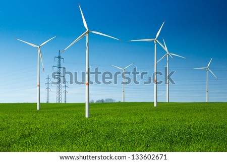 Wind turbine as renewable energy source, electricity pylon, wiring,  summer landscape with clear blue sky and green meadow