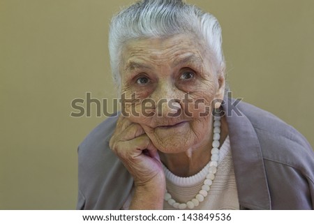 old lady\'s portrait in front of a light brown wall