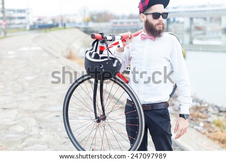 Young bearded man with sunglasses holding a red bike.