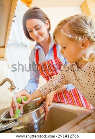 Beautiful mother with cute little daughter preparing food in the kitchen.