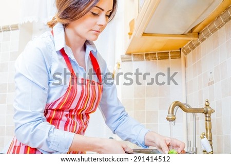 Gorgeous lady in the kitchen watering fresh vegetables.