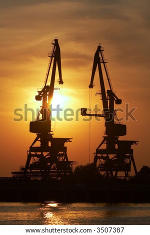 Silhouette of an industrial dock crane unloading at sunset