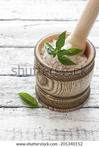 Wood mortar with salt and basil over white wood background
