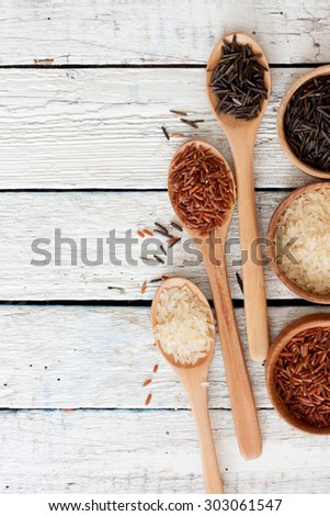 Red, black, white rice in wood bowls and spoons over white wood background