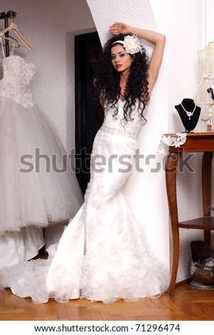 Brunette bride with long and curly hair posing in bridal shop