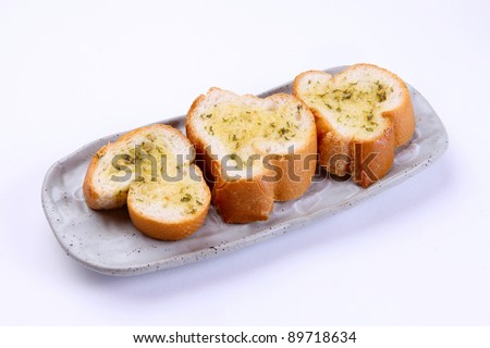 Garlic bread with herbs, on white bread dish.