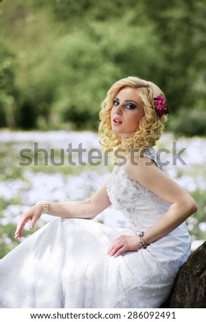 Beautiful young bride in white dress sits on tree in summer green park