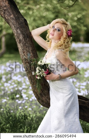 Beautiful young bride in white dress with bouquet near tree in summer green park