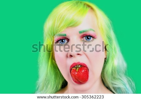 Beautiful girl with color hair holds strawberry with lips on green background
