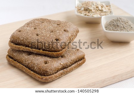 two pieces of rye bread square shape and rye bran and muesli on plates on wood background with selective focus
