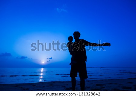 silhouette of happy man playing with daughter at the beach.