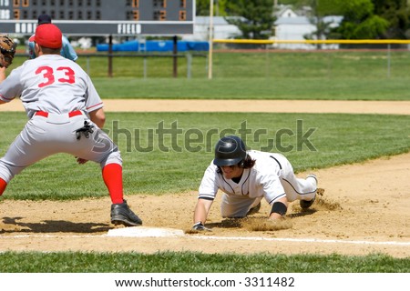 Baseball player dives back to first base as a pickoff attempt is made. Scoreboard in the background.