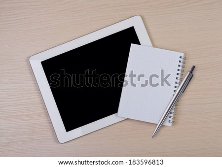 Tablet computer with note pad and pen on wooden desk