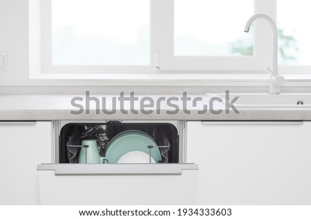 Opened door of build-in dishwasher on modern kitchen counter background
