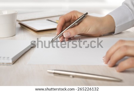 Closeup of business woman hand writing on paper at desk