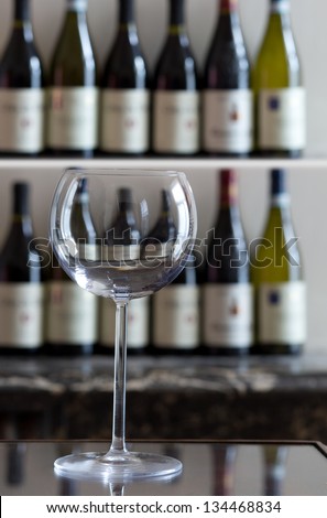 Large wine glass with bottles of wine in the background