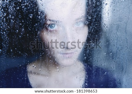 young melancholy and sad woman portrait behind the window in the rain with rain drops on it