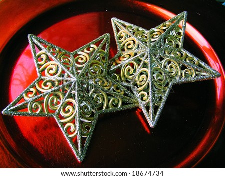 cross-process photographic reproduction/close up of two christmas stars on a red metallic plate