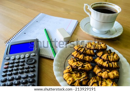 workplace, study place with calculator (with blue box), workbook, cup of coffee and cookies - stock photo