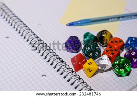 open exercise book with sticky card, pen and role playing dices - stock photo